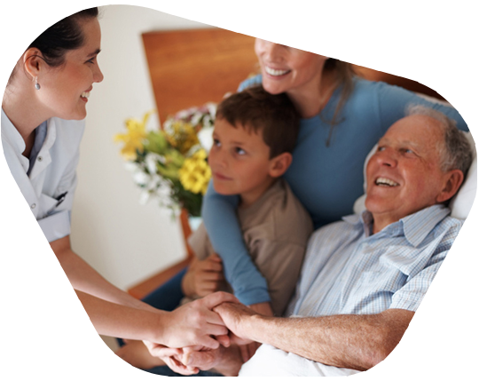 Krankenpflegerin kümmert sich um einen älteren Mann im Bett, der von Familienangehörigen besucht wird.